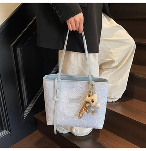 Détail du cabas bleu clair avec broderie florale blanche et breloque ours en peluche