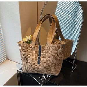 Detail of hand-woven straw tote bag with black leather strap and metal buckle