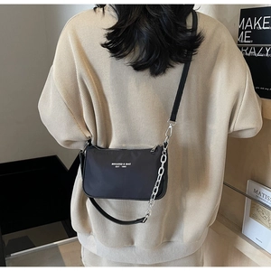 Detail of black nylon crossbody bag with silver chain strap on cream knit sweater