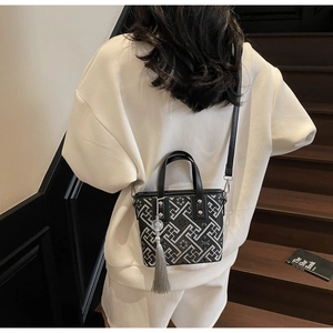 Détail du sac seau noir avec motifs géométriques gris et pompon en soie sur escalier