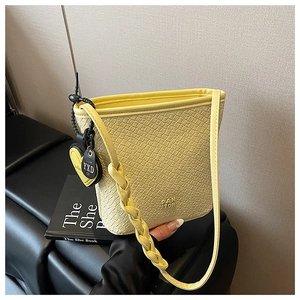Détail du sac seau jaune avec texture croco, bandoulière tressée et breloque cœur