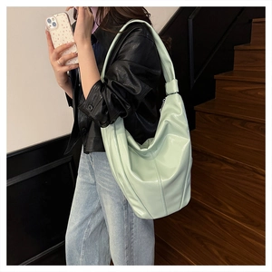 Détail du sac seau en cuir vert menthe avec large bandoulière nouée et aspect brillant