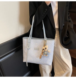 Détail d'un sac cabas matelassé bleu clair avec motifs floraux et pendentif ours