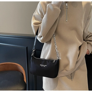 Close-up of black nylon shoulder bag with silver chain strap and white printed logo