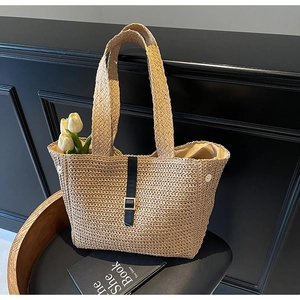 Detailed macro view of beige woven straw tote bag with navy straps and metal buckle