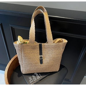 Macro detail of hand-woven straw tote with black leather strap and metallic buckle