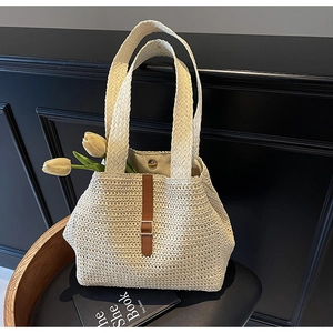 Detail of woven straw tote bag with brown leather buckle strap on black chair