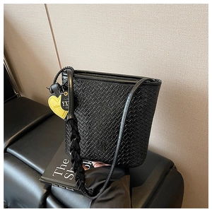 Détail du sac seau tressé noir avec bandoulière et pendentif en forme de cœur jaune