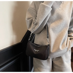Detail of black nylon shoulder bag with chain strap and MIKAXIQI branding on gray outfit