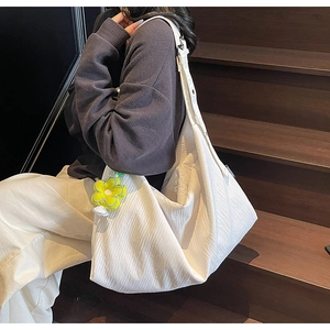 Detail of white pleated fabric shoulder bag with yellow flower charm on wooden stairs