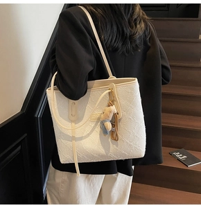 Détail du cabas texturé crème avec breloque ours porté par un mannequin élégant