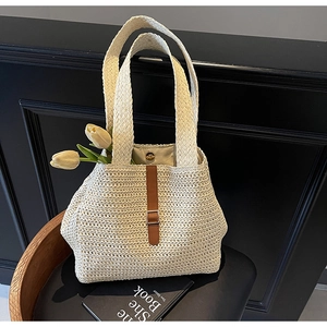 Detail of a woven straw tote bag featuring brown leather buckle and magnetic closure