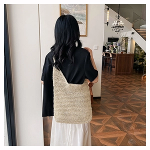 Detailed view of cream woven straw tote bag held by model in a cozy interior setting
