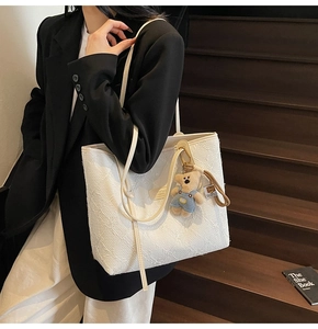 Sac cabas blanc gaufré avec charme d'ours, porté avec un costume noir par un mannequin