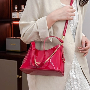Close-up of red patent leather bucket bag with gold chain and crossbody strap on a model