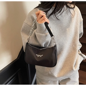 Model showcasing a black crescent nylon shoulder bag with silver chain and brand logo