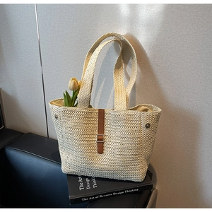 Detail of woven straw tote bag with brown leather strap and metal buckle on leather seat
