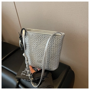 Détail du sac seau tressé argenté avec texture métallique posé sur un banc en cuir