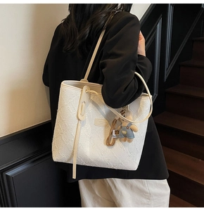 Détail d'un sac cabas blanc à texture gaufrée avec un charmant pendentif ours en peluche