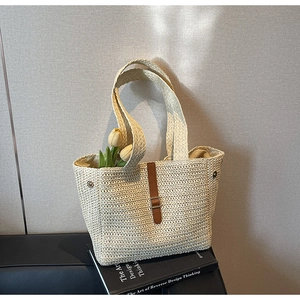 Detail of hand-woven straw tote bag with leather strap and metal buckle on book