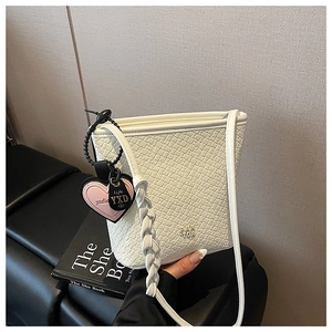 Détail du sac seau blanc tressé avec breloque cœur et bandoulière assortie sur du cuir