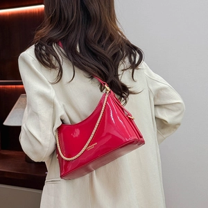 Detail of a bright red patent leather handbag with golden chain strap and mirror finish