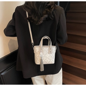 Détail du sac seau crème minimaliste avec motifs géométriques et pompon gris