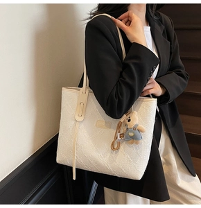 Détail du sac fourre-tout blanc texturé avec un charme d'ours et une étiquette en cuir