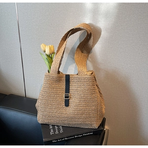 Detailed close-up of woven straw tote bag featuring blue leather trim and metal buckle