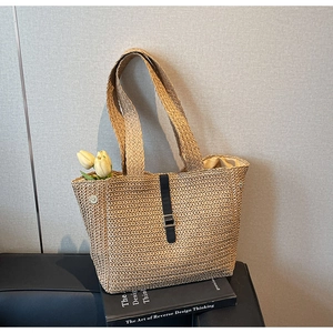 Detail of woven straw tote bag with black leather strap and silver buckle on a book