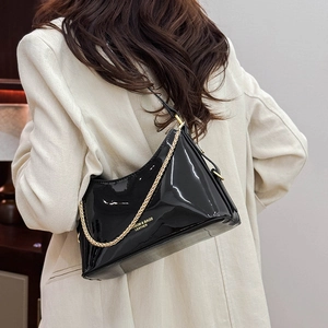 Detail of glossy black patent leather shoulder bag with gold chain and printed logo