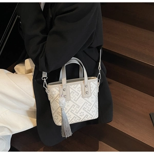Détail d'un sac fourre-tout en jacquard crème avec pompons gris porté par un mannequin