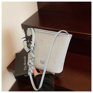 Détail du sac seau tressé bleu clair avec breloque cœur sur un fond en bois