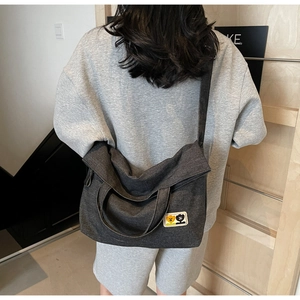 Detail view of large dark grey denim crossbody bag with cute cartoon patch and folded top