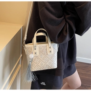 Détail du sac seau beige avec motifs floraux en jacquard gris et pompon décoratif élégant
