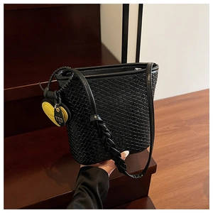 Détail du sac seau noir tressé avec un charm de cœur jaune et une bandoulière longue