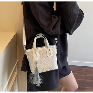 Close-up of cream bucket bag featuring geometric texture and long silk tassel detail