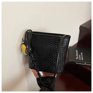 Détail d'un sac seau tressé noir avec une breloque cœur en cuir jaune éclatant