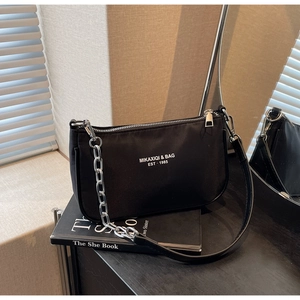 Close-up of black nylon shoulder bag featuring silver chain detail and white logo print