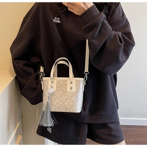 Detail of cream bucket bag with geometric embossing and stylish grey tassel accent