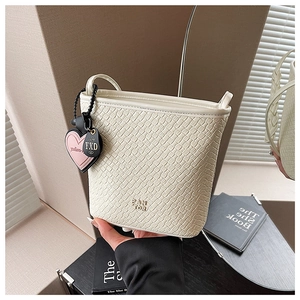 Détail du sac seau tressé crème avec breloque cœur et texte gaufré sur le bas