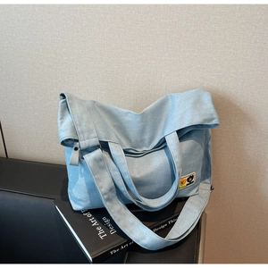 Detail of light blue denim tote bag with cartoon patches resting on design books