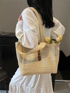 Woven straw tote bag with brown leather buckle detail carried by a model in white dress
