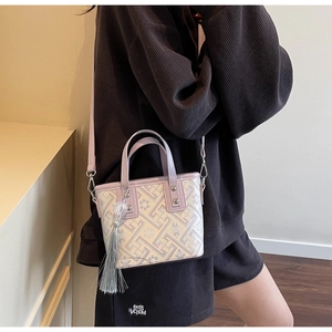Détail du tissu jacquard floral et du pompon gris sur un petit sac à main seau