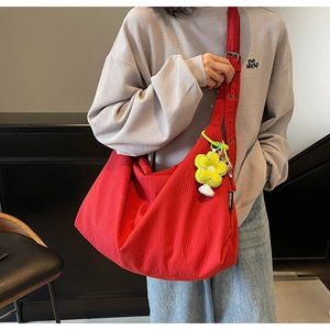 Close-up of red pleated tote bag with yellow flower pendant worn on shoulder