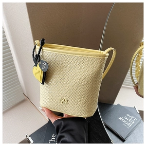 Détail du sac seau jaune pâle à texture tressée avec pendentif coeur et logo