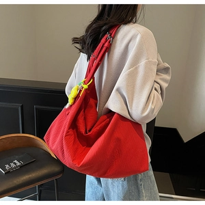 Large red pleated fabric tote bag with a yellow cartoon charm worn as a crossbody bag