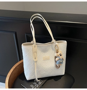 Détail du sac cabas blanc texturé avec logo et breloque ours en peluche bleu