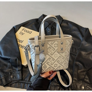 Gros plan d'un sac jacquard beige avec pompon gris posé sur du cuir noir