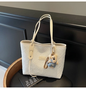 Détail du sac cabas beige gaufré avec étiquette de marque et breloque ours en peluche